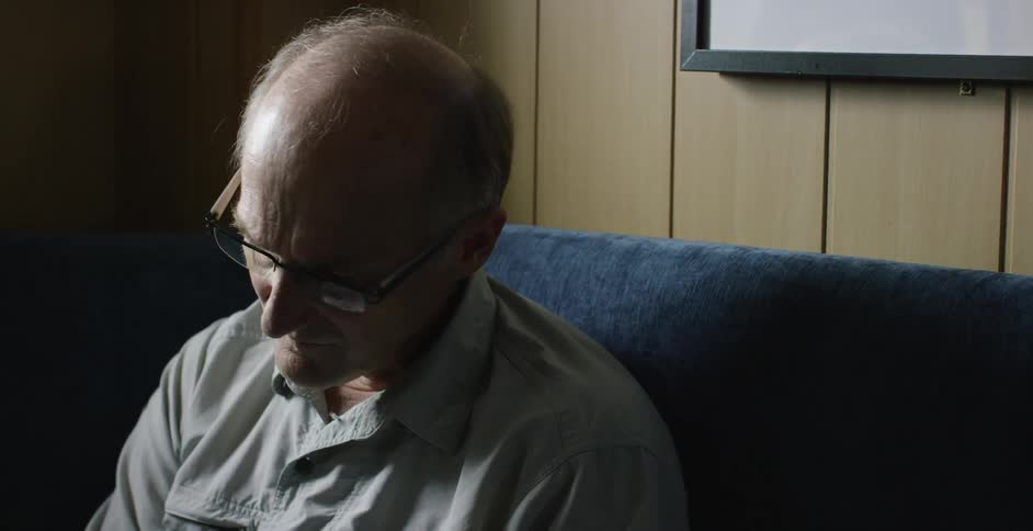 An elderly man sits on a couch reading