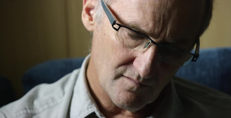 A man in glasses stares down sitting on a couch