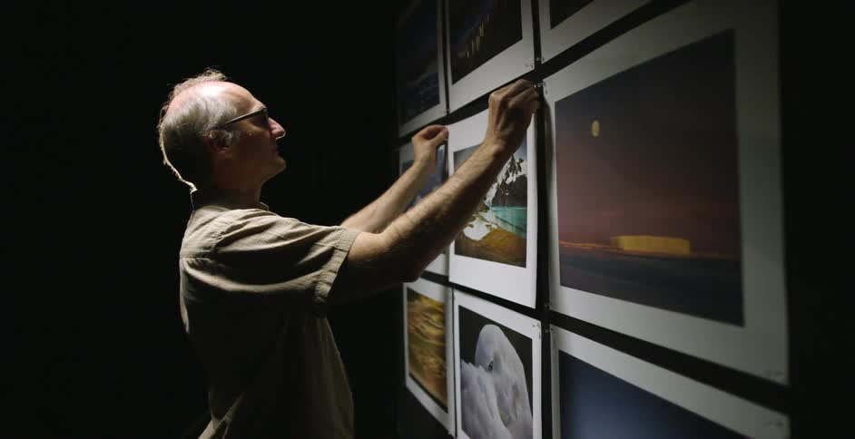 A man hangs up photographs in a dark studio