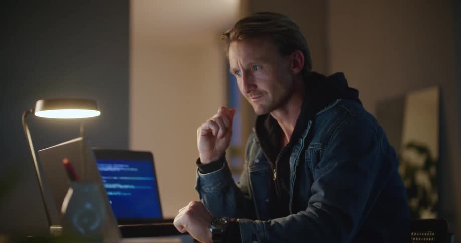 A man works on lines of code while sitting at his desk at home
