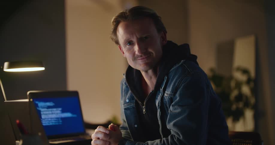 Man sitting at desk with two computers turns and smiles