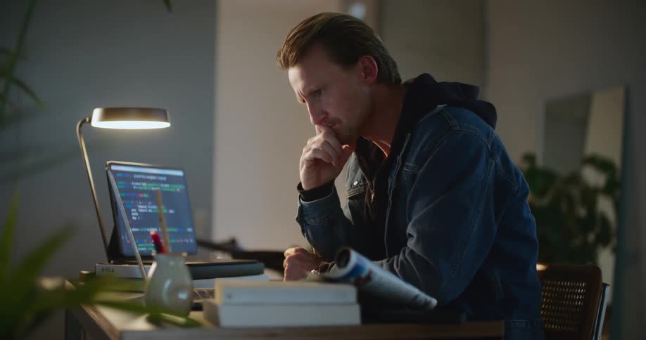 Man jots on magazine after typing on one computer and consulting two computer screens