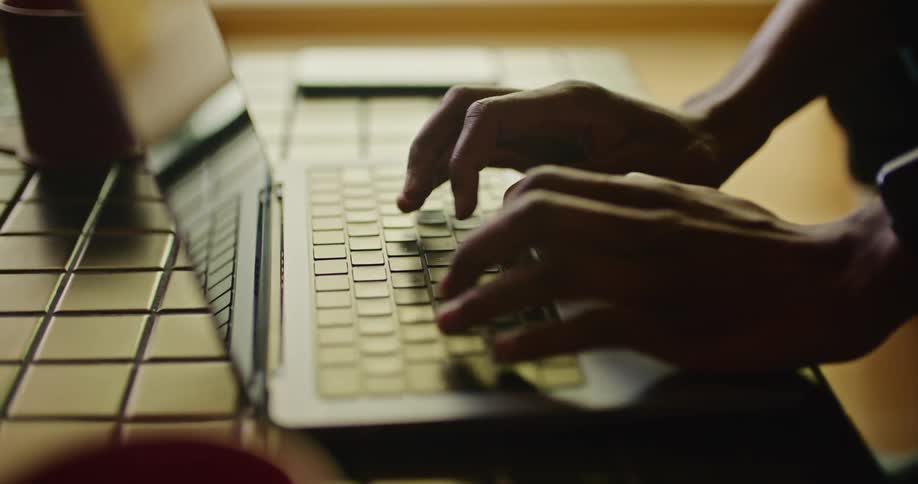 A man is typing on the keyboard of a laptop computer