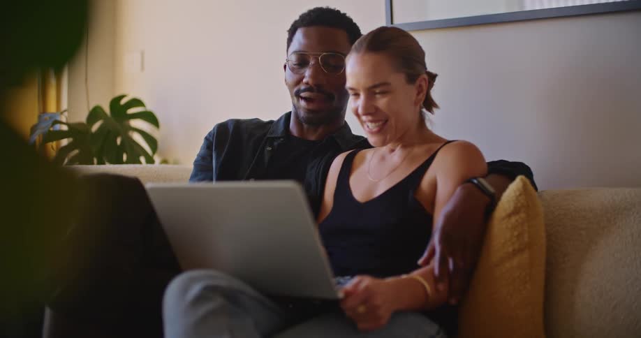 A man kisses his partner on the cheek while they look at a laptop together