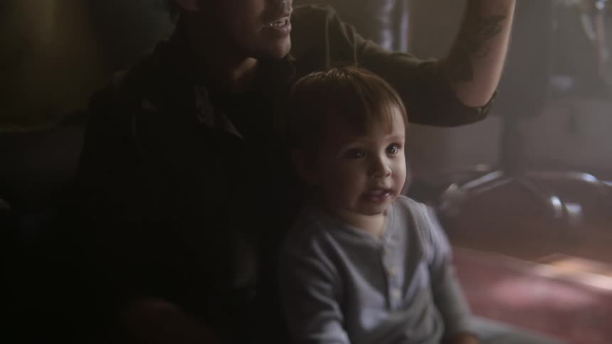 Toddler son sits on fathers lap in room