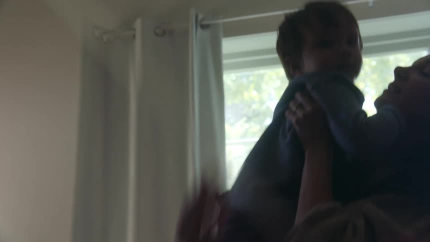 A little boy runs up to his mother as she picks him up and he points to something behind him