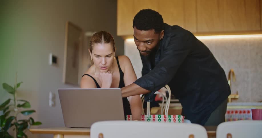 A man stands behind his girlfriend while they look at a laptop together