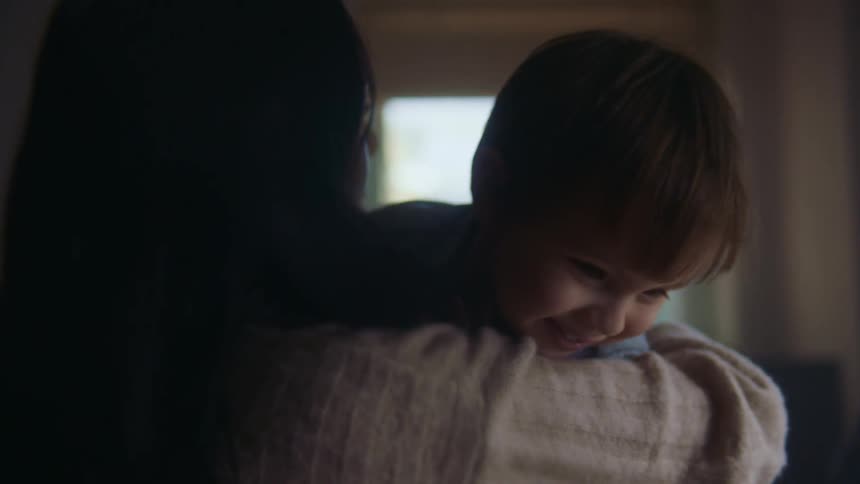 A woman holds a young boy over her shoulder and he talks while smiling