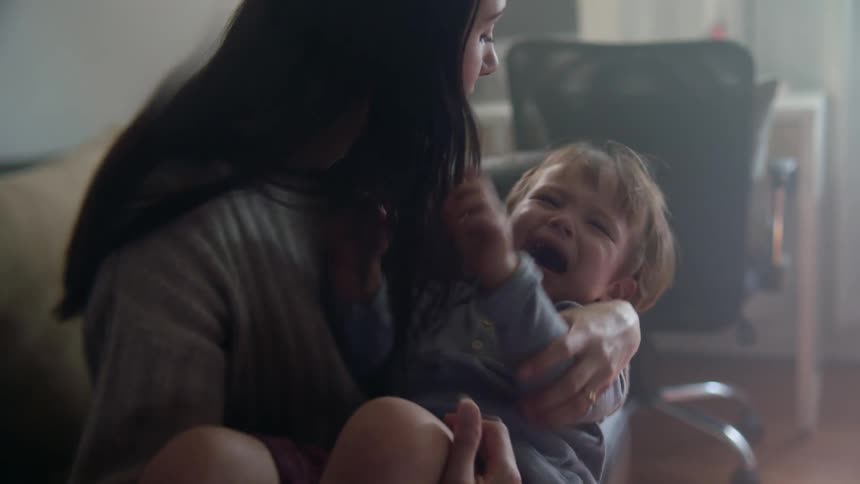 A mother holds her son in her arms as he cries and pushes her away