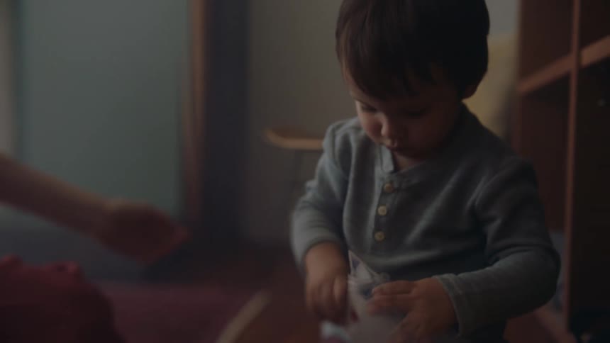 A little boy sitting on the floor picking cards up off it and putting them into a cup he is holding