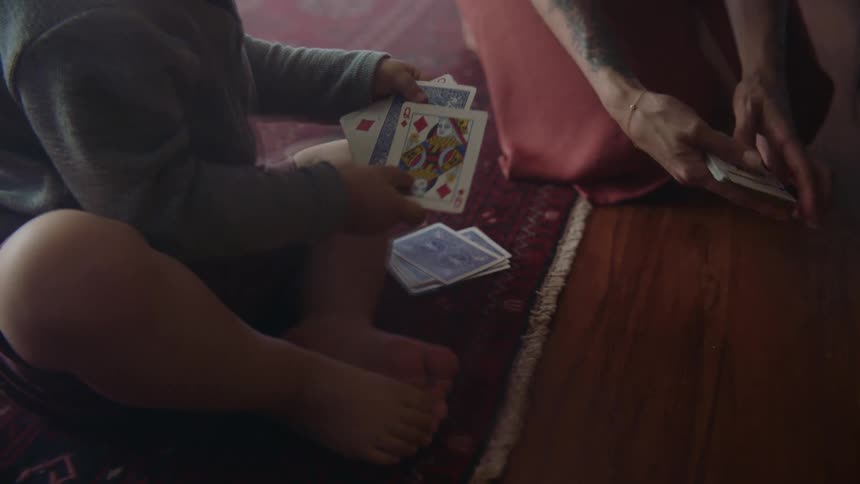 A little boy picking up cards off the floor with his mother next to him
