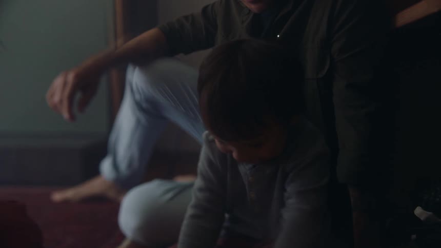 A little boy sitting on the floor pouring cards out of a cup while his father and mother sit around him on the floor