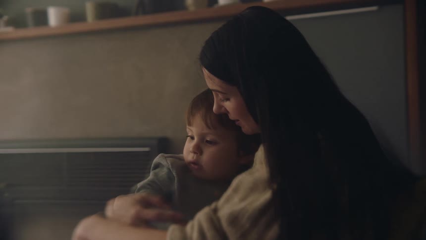 A mother sits rocking her son side to side in her arms while she talks softly to him