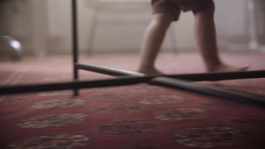 A small child walks barefooted while indoors and navigating around furniture