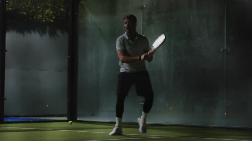 A young man is playing tennis outdoors at night time