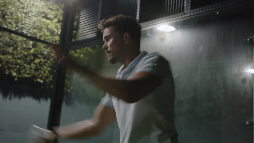 A man swings a paddle used to play pickle ball while outdoors at night