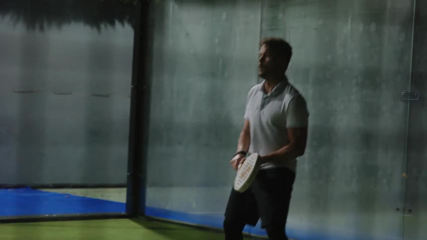 Man in light blue polo shirt and black shorts plays tennis on court