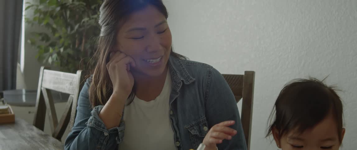 Close up of a happy mother smiling while watching her daughter eating at the dining table