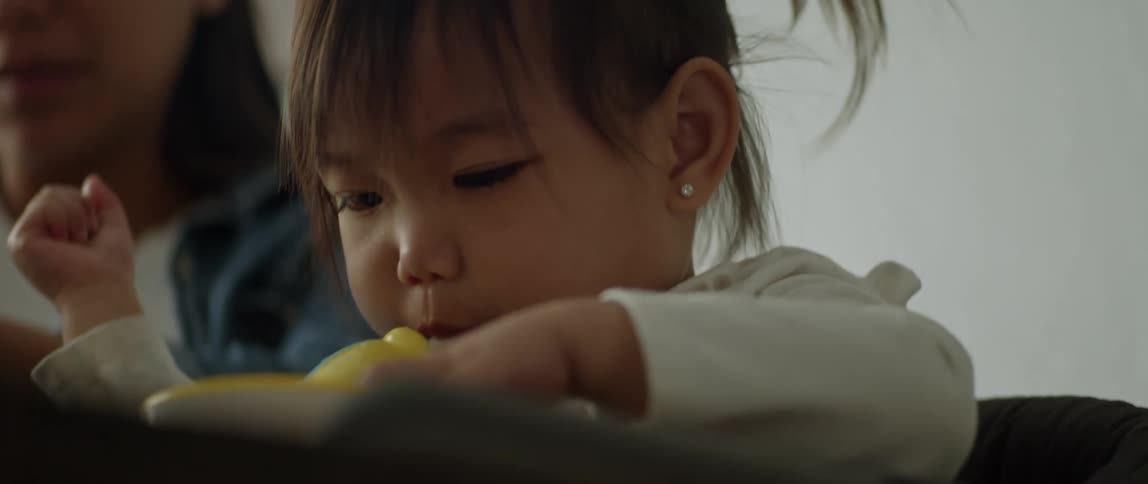 A woman gives fruit to her daughter while the girl drinks from a sippy cup
