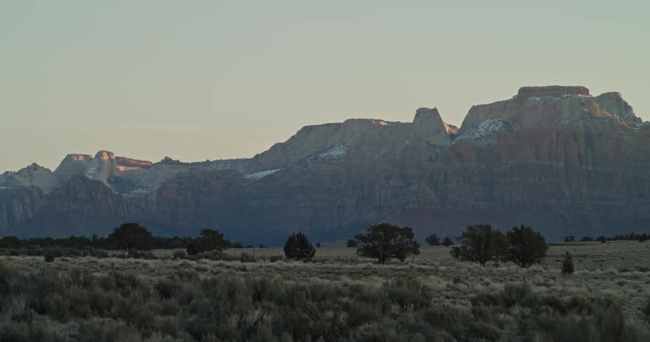 Grasslands sit underneath towering red rock mountains at dawn