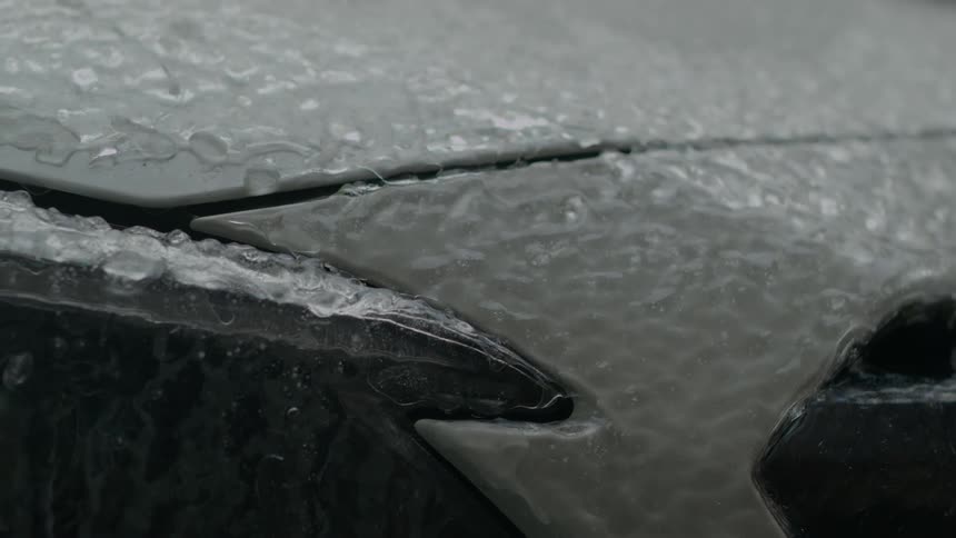Close up of water droplets running down the melting ice on the hood of a white car