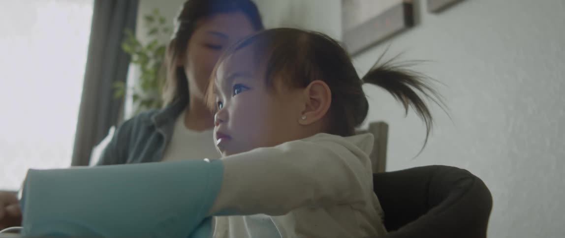 A mother sitting next to her young daughter at the dining table stands up and walks away