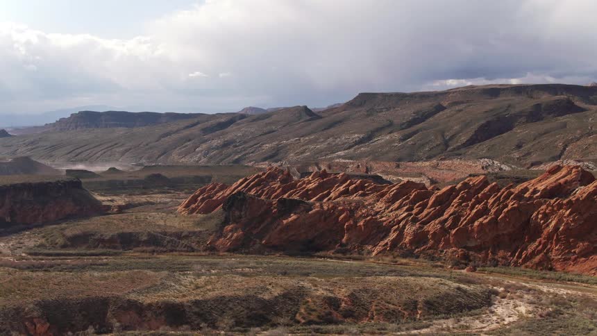 Red rock formations surrounded by mountains under a cloudy sky