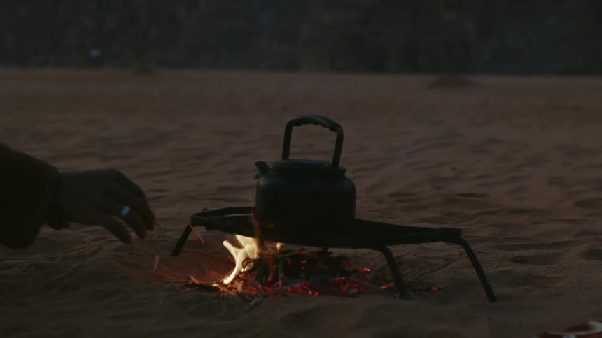 Hand of a person adding coals under a grill to boil water on a teapot in the beach