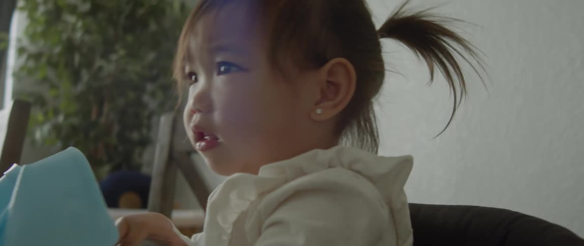 A young girl sits in a highchair while playing with the napkin in front of her