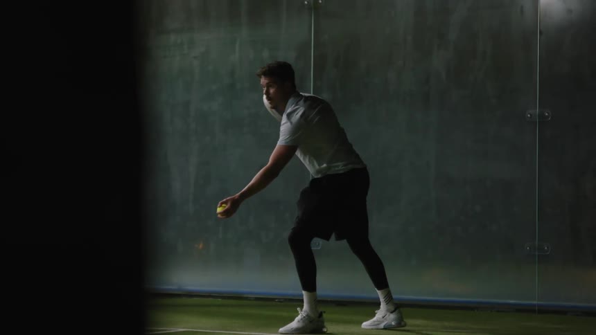 Man with gray shirt black pants and white shoes play tennis in the tennis court hitting the ball with racket
