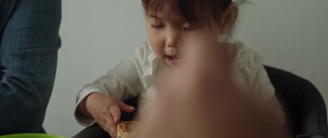A little girl sitting at a table next to people while she examines the food in front of her