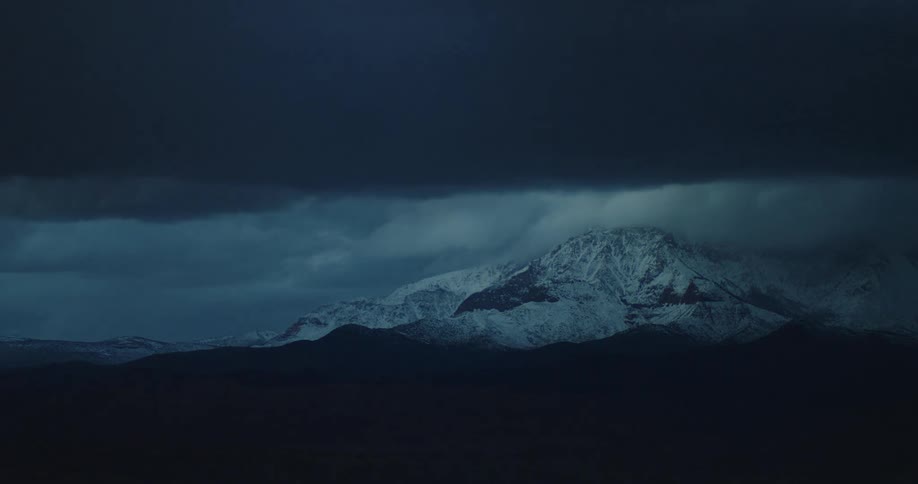 Dark storm clouds dump snow over desert mountain range at dusk
