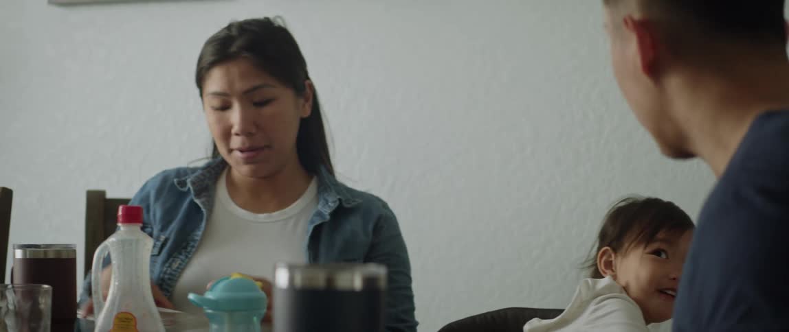 A mom and dad are eating breakfast at home with their young daughter and she is playing with a fork at the table showing it to her dad