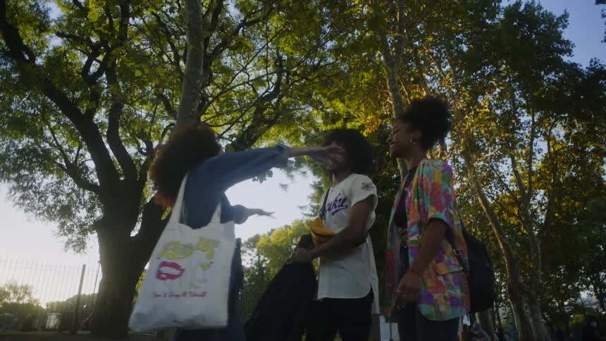 A woman sitting on a sidewalk then standing up to greet to friends walking up to her
