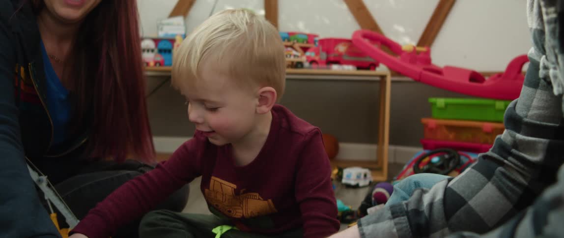 Two adults are playing toys with a young boy while seated on the floor