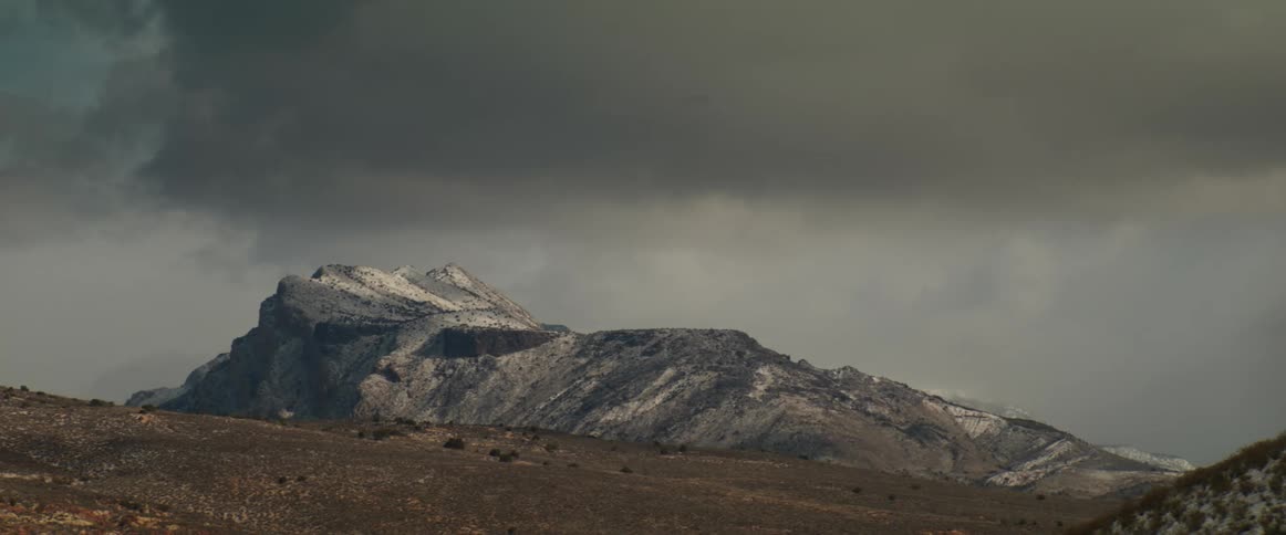 A dark storm cloud floats over a mountain and casts a shadow on the ground as it moves