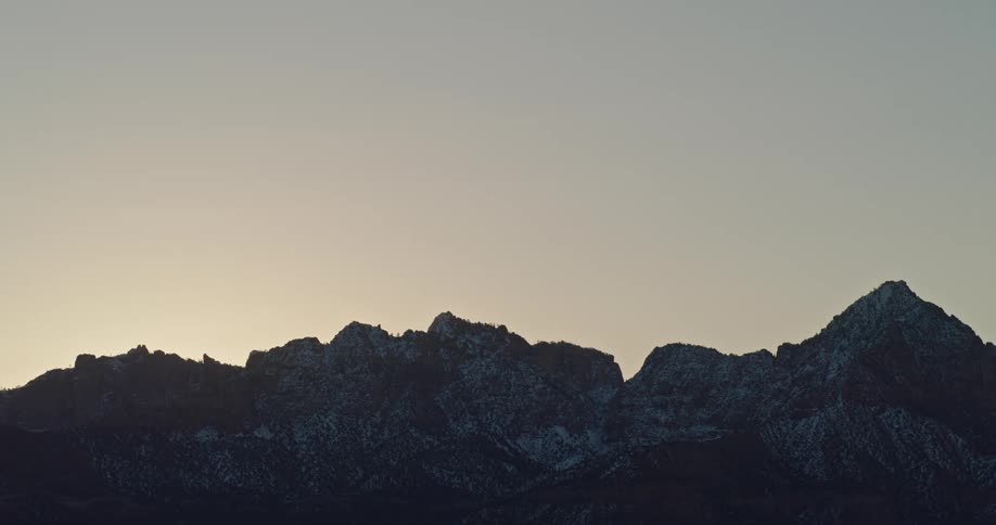 The silhouette of a snow dusted mountain range at dawn