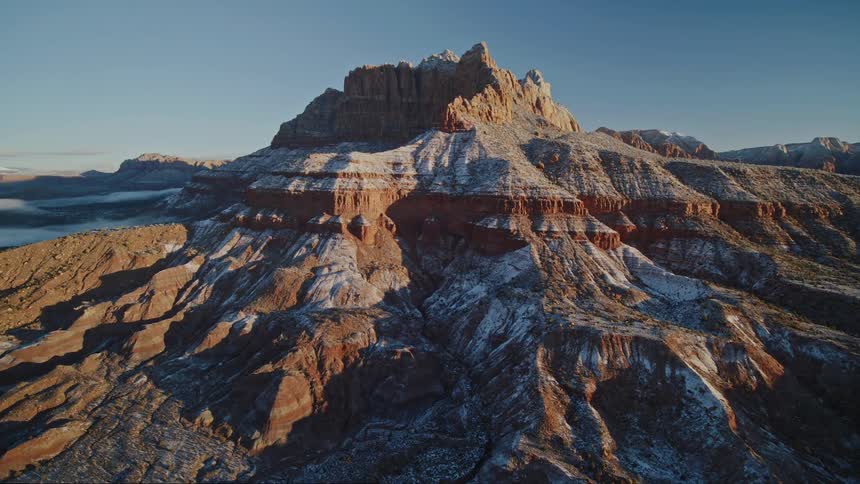 Aerial reveal of a red rock mountain and ridges covered in a dusting of snow at dawn
