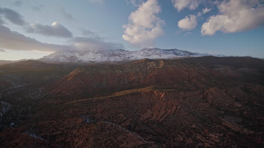 Orbital aerial view of distant snow covered red rock mountain peaks in the evening