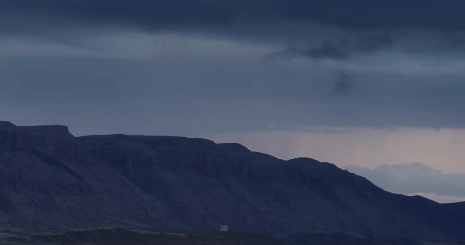 Storm clouds loom over desert mountains in the evening