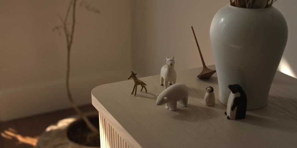 A closeup of a wood end table with a vase and animal figurines on it while a persons shadow moves across it