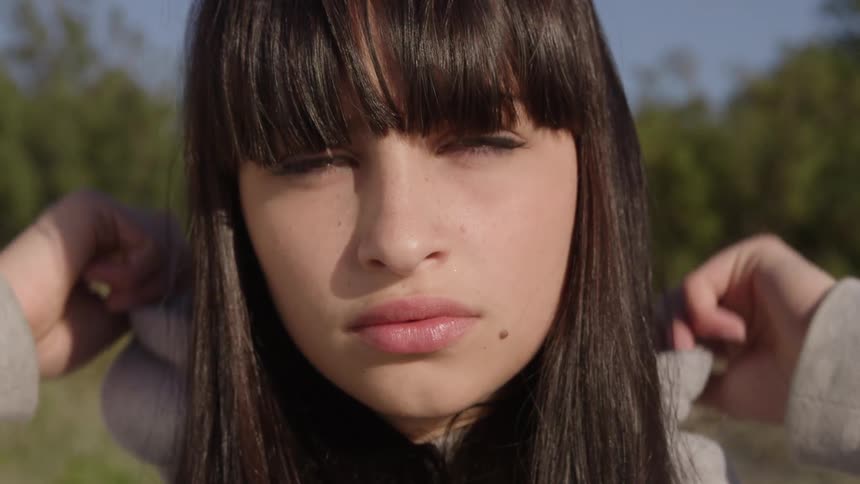 Close up of the face of a young woman in a hoodie standing outdoors looking at the camera