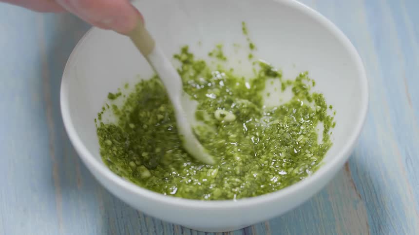 Person stirs green sauce in white bowl
