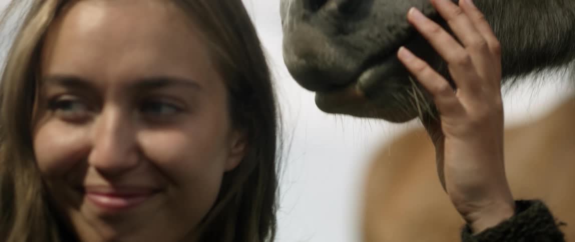 A woman smiles while petting a horse