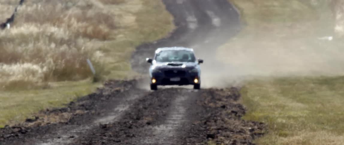 A vehicle driving on a dirt road raising dust surrounded by grass