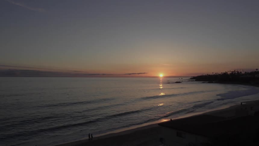 People walk on a beach as the sun sets