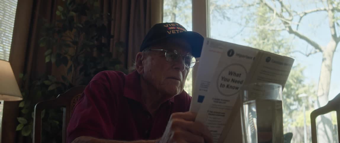 An elderly man sits at home and reads a newspaper