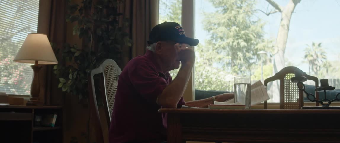 An elderly man is sitting down and reading the paper