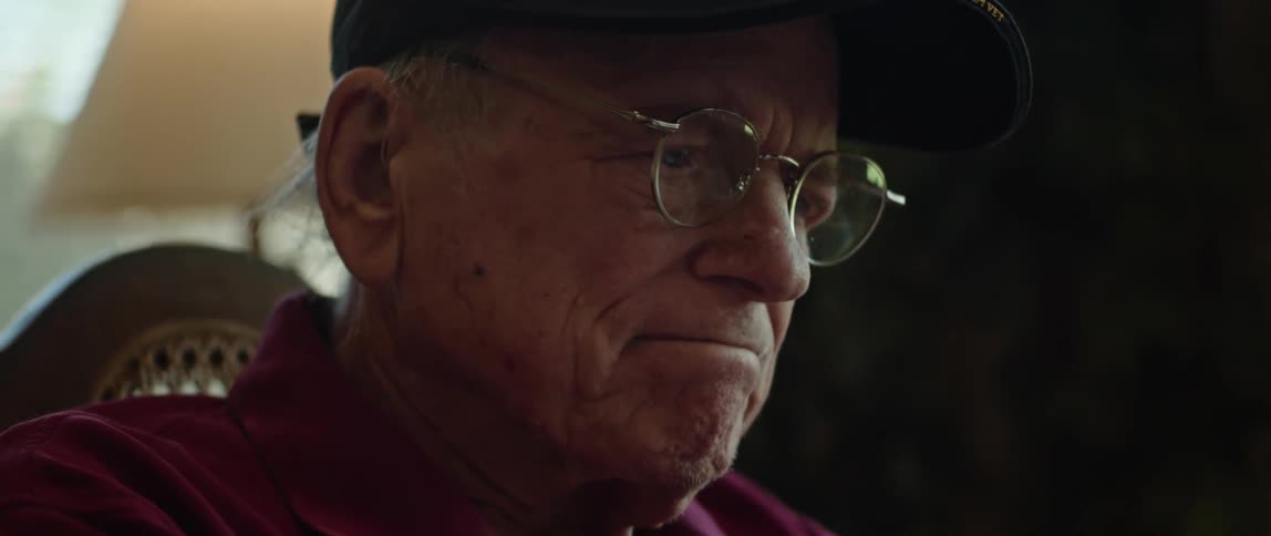 Elderly man sitting in chair shakes his head while frowning