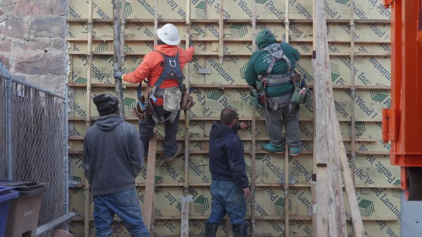 Two men standing below two men on a wall they are building